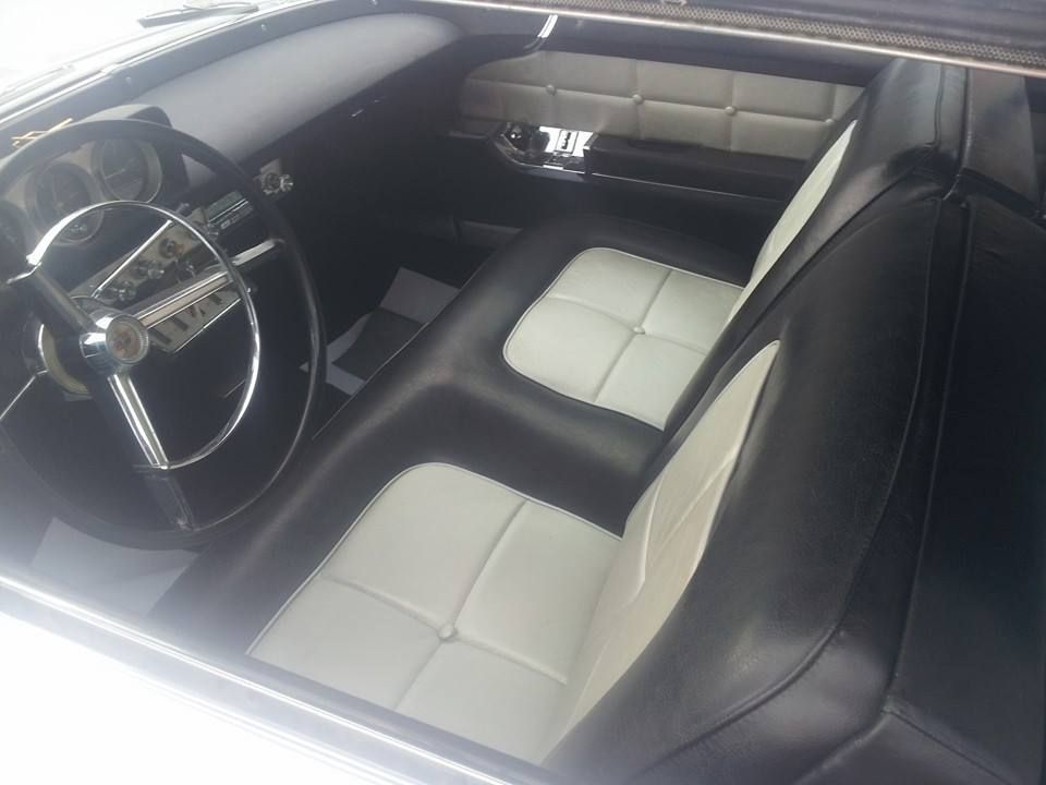 Interior of a classic car featuring a black and white bench seat, chrome-accented steering wheel, and dashboard.