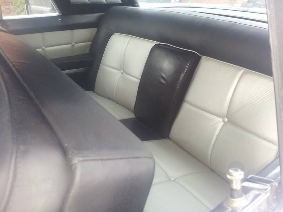 A car backseat featuring black and white tufted leather upholstery with a center armrest.