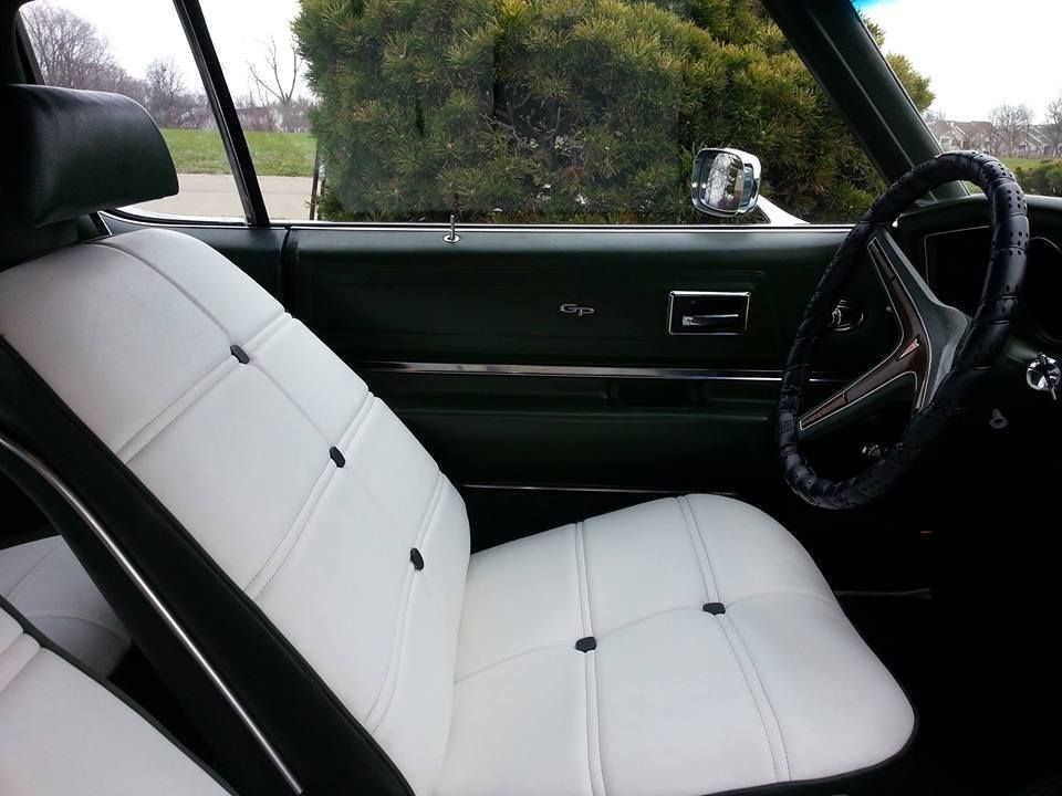 The interior of a classic car featuring white tufted vinyl bucket seats, a black dashboard, and a black steering wheel.
