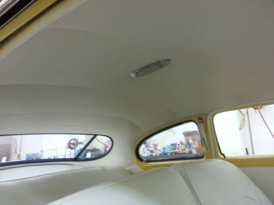 Interior of a vintage car with light-colored headliner, rear bench seat, and back windows with yellow door trim.