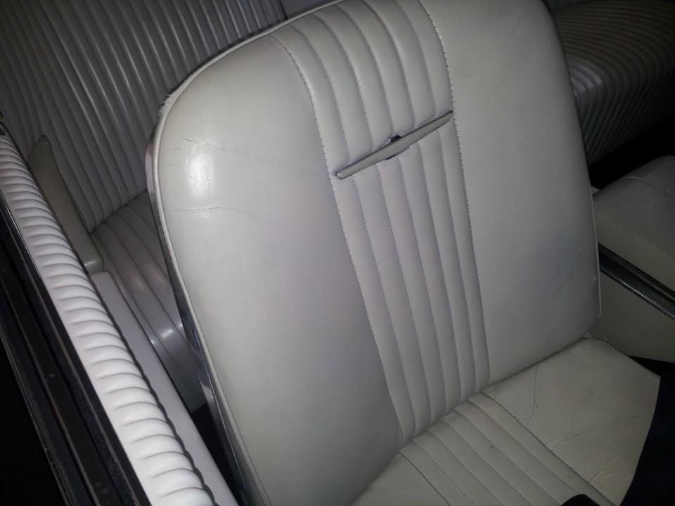 Light gray, pleated leather bucket seat with a chrome horizontal accent emblem inside a vintage vehicle.