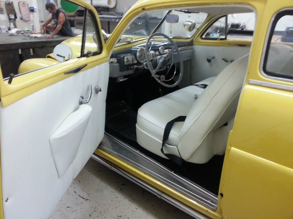 A yellow vintage car interior with a white leather door panel and seat, viewed through the open driver-side door.