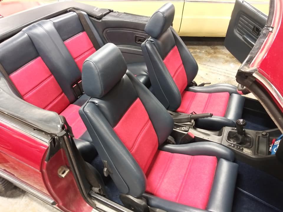 Interior of a red convertible with dark blue and bright pink upholstered front and rear bucket seats.