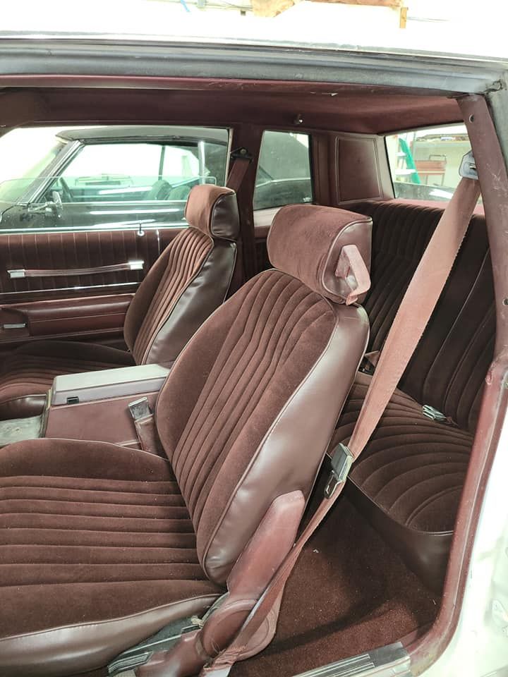 The interior of a classic car with two-tone brown cloth and vinyl bucket seats and matching maroon carpet.