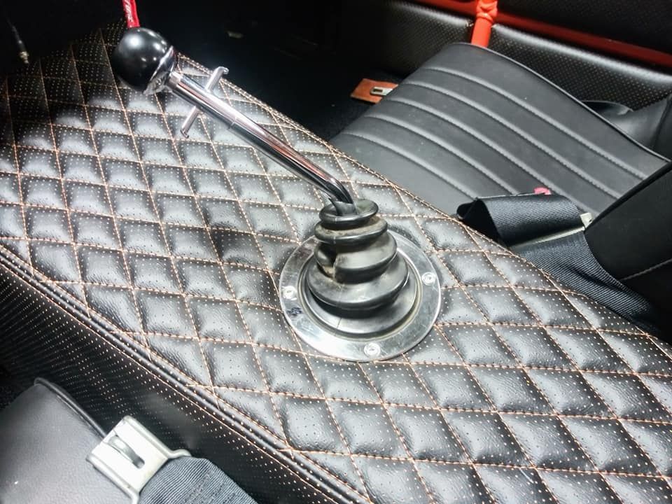A car's interior featuring a black quilted leather center console, a metal gear shifter with a round knob, and seat belts.
