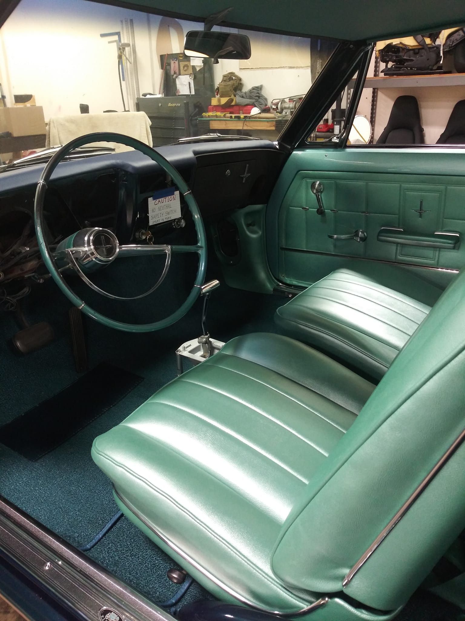 The interior of a classic car featuring mint green vinyl bucket seats, a matching steering wheel, and a shifter console.