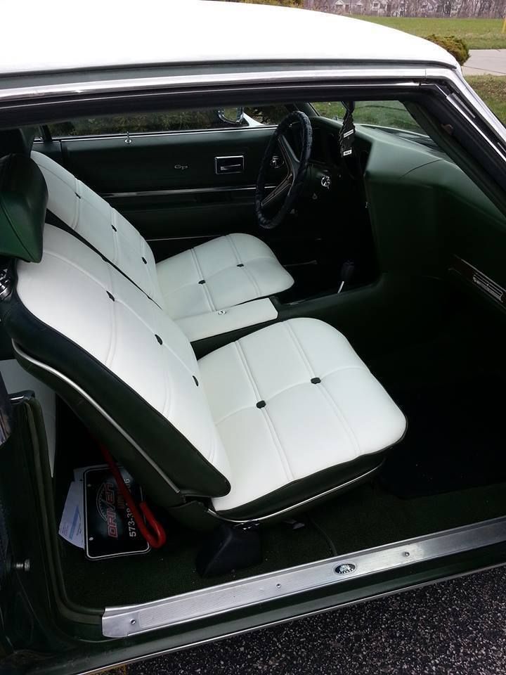 Interior of a classic car featuring white vinyl bucket seats with dark green trim and green carpeting.