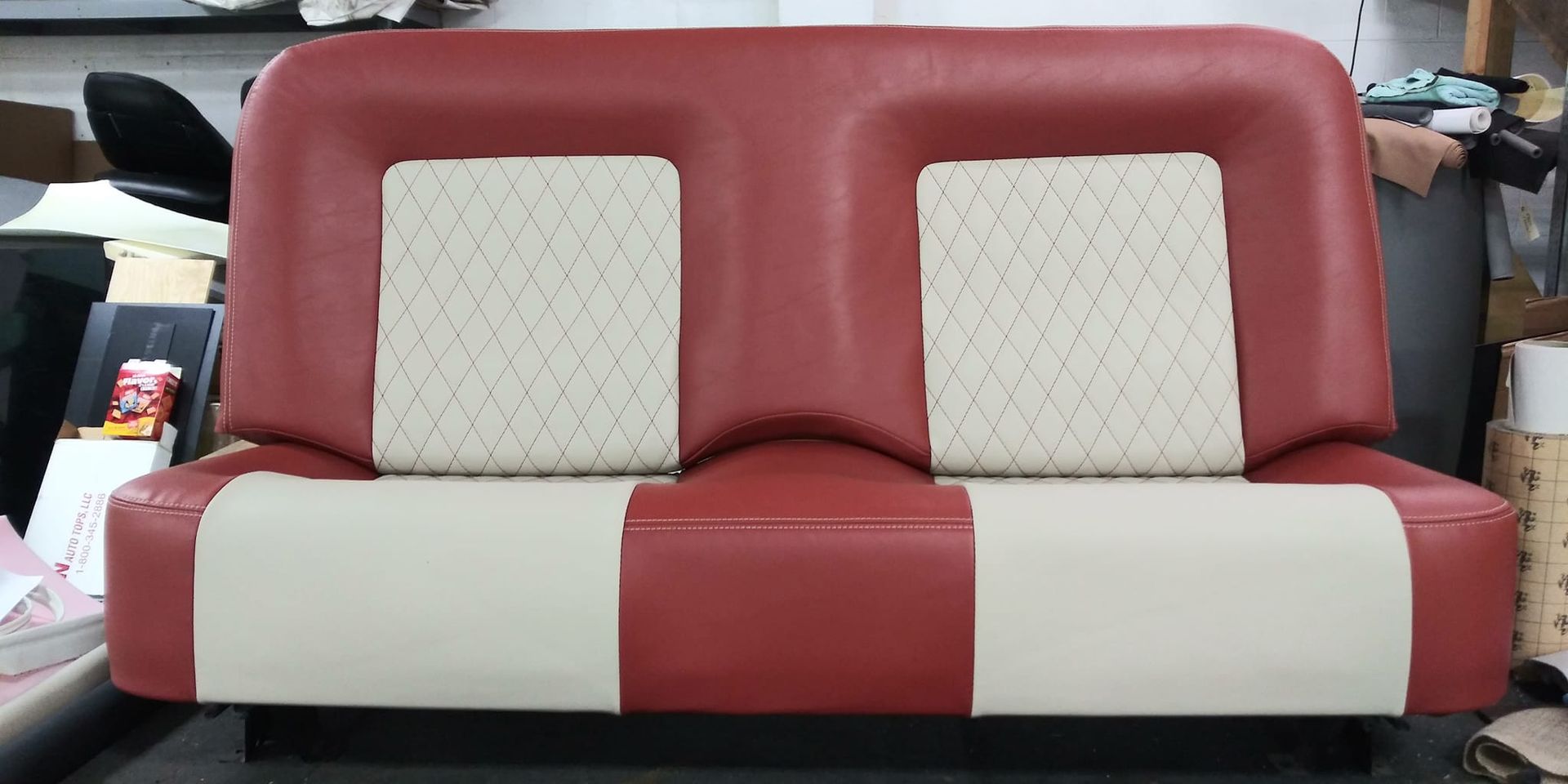 A dual-seat bench with red vinyl sides, cream-colored base cushions, and two square, diamond-stitched cream back cushions.