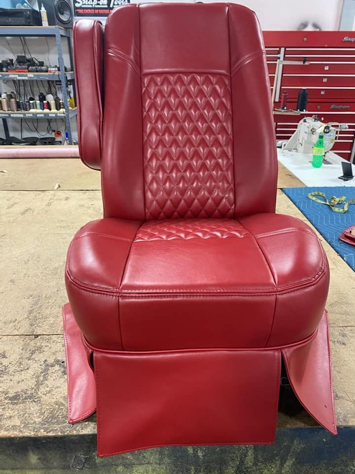 A red upholstered captain's chair with diamond-stitched detailing, set in an auto upholstery workshop.