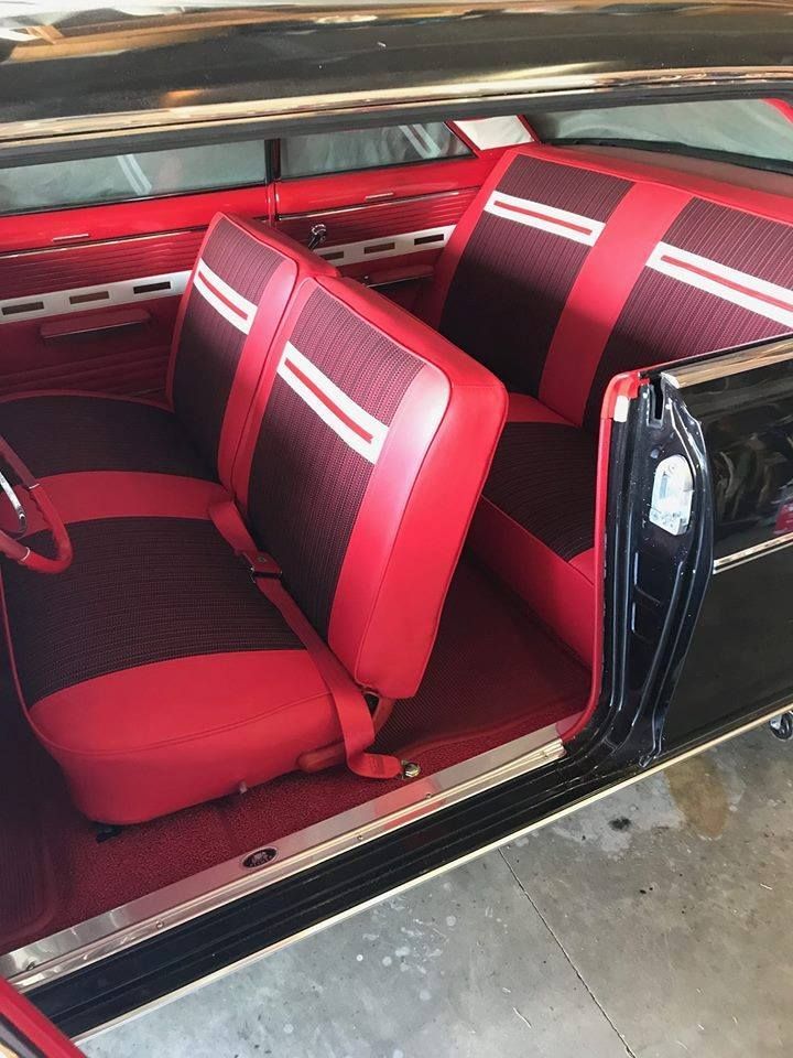 A classic car interior with two-tone red and dark red vinyl bench seats, a matching red floor, and metal trim.
