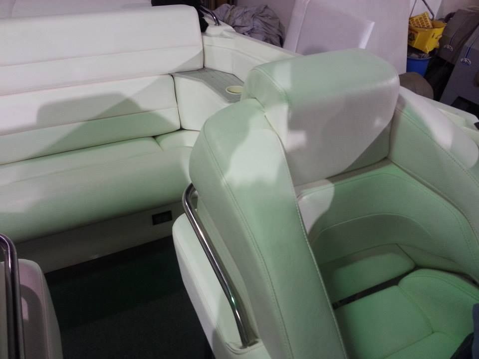 Interior view of a boat featuring white upholstered bench seating and a matching captain's chair with a metal grab bar.
