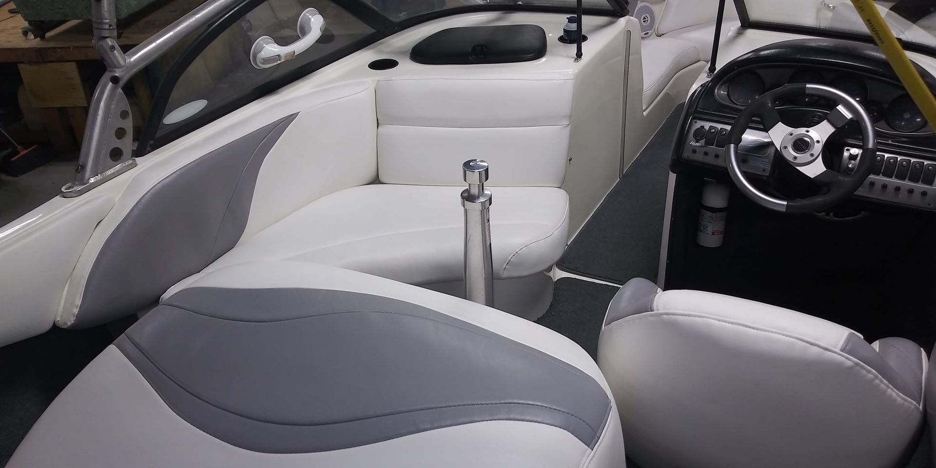 Interior of a motorboat featuring white and gray vinyl seats, a steering wheel, and dark gray flooring.