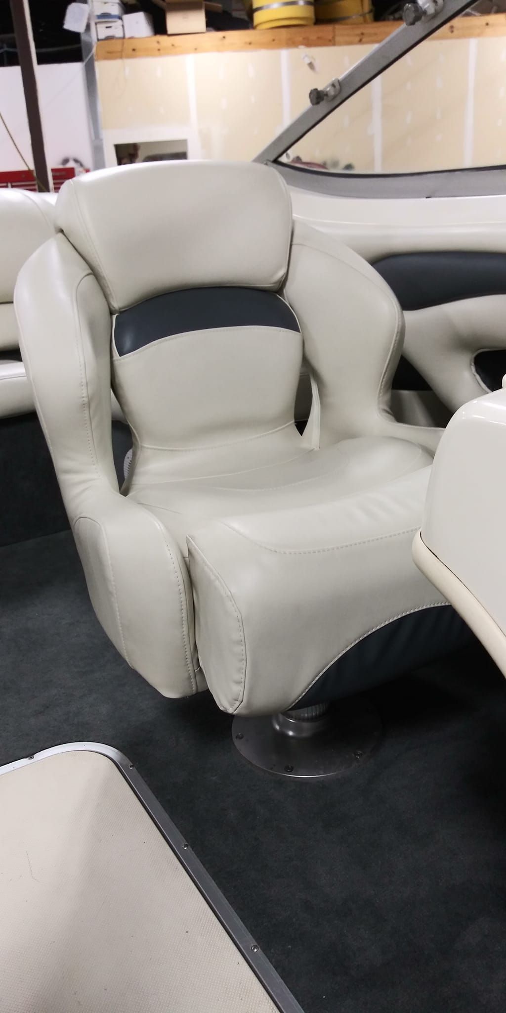 A white and navy blue bucket-style marine captain's chair inside a boat, mounted on a pedestal base.