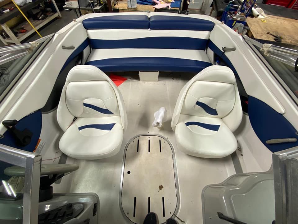Interior of a boat with two white bucket seats, blue and white upholstered bench seating, and a floor storage hatch.