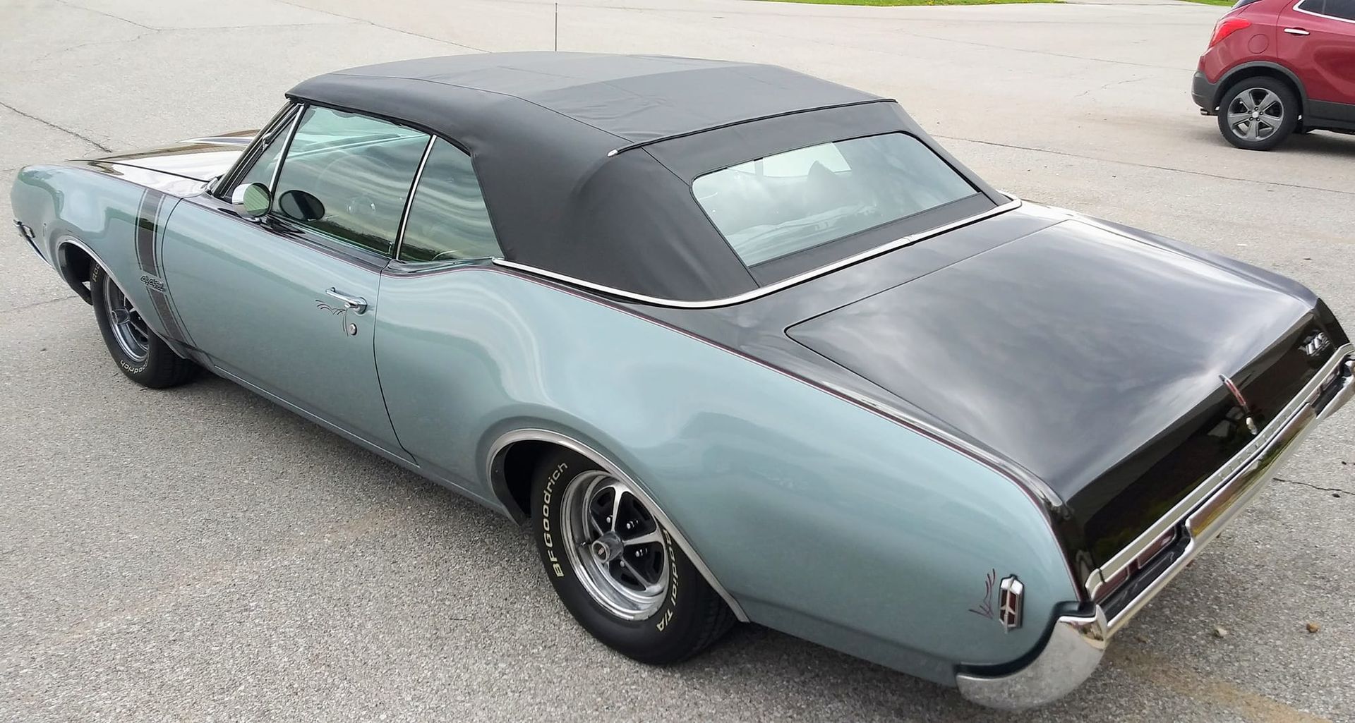 Light blue vintage convertible with a black soft top and trunk lid, parked on an asphalt surface.