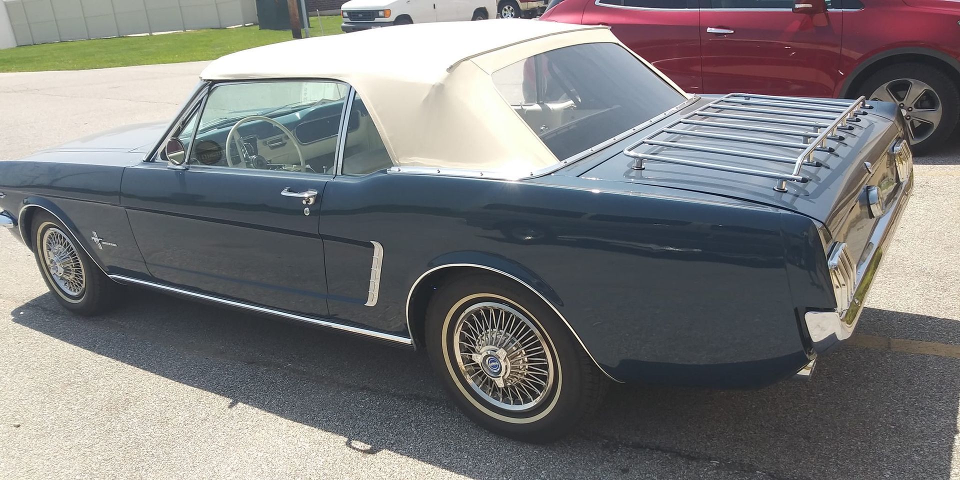 A dark blue classic Ford Mustang convertible with a white top and wire wheels parked in a lot.