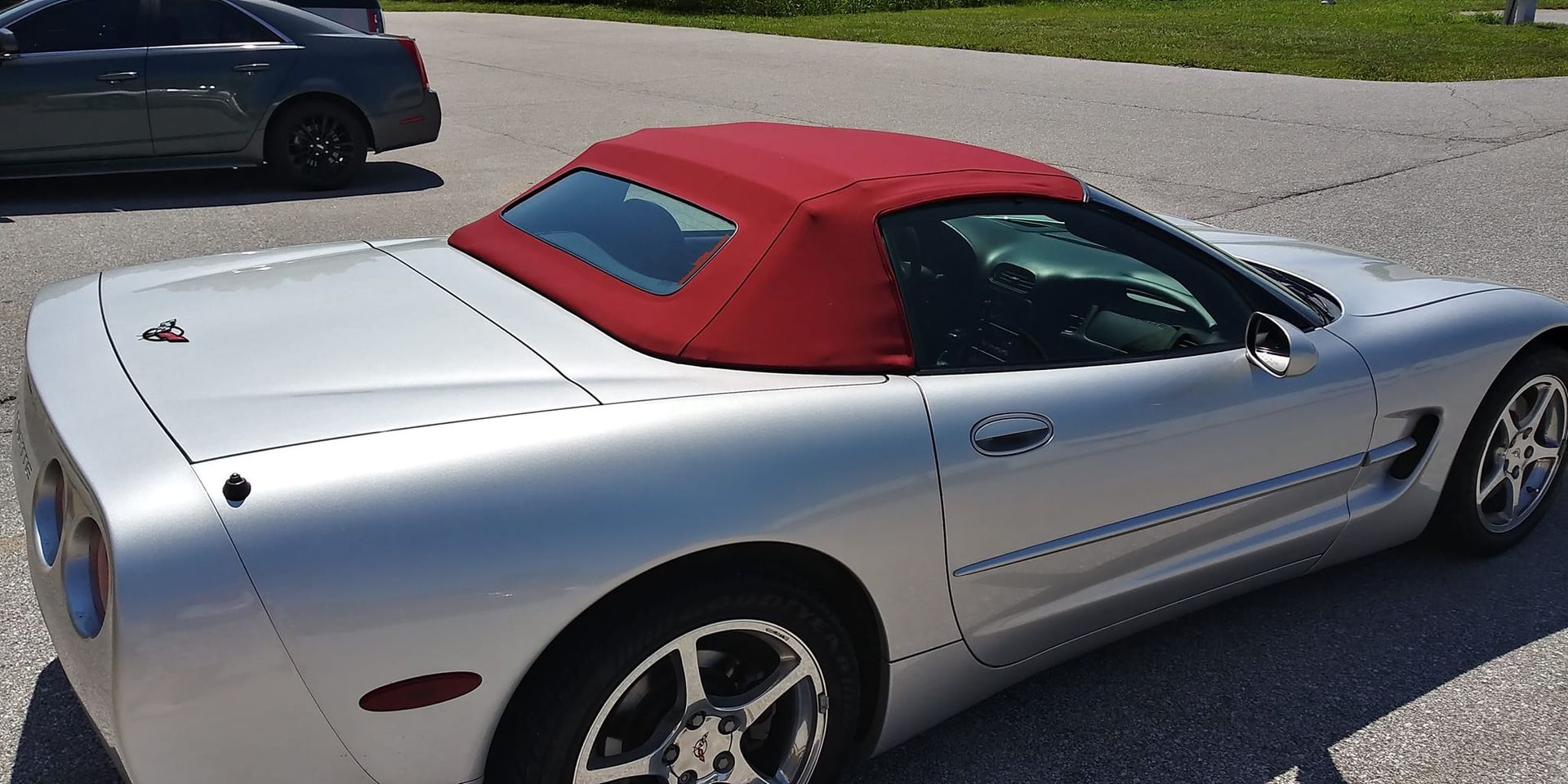 A silver Chevrolet Corvette convertible with a red soft top parked on an asphalt lot.