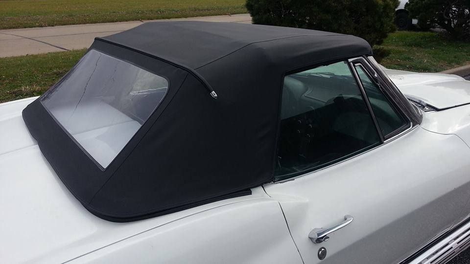 A close-up, high-angle shot of a white convertible car with a closed black soft top and clear rear window.
