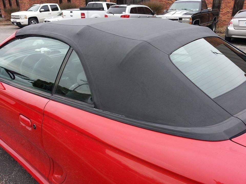 A close-up view of the black canvas convertible roof and rear window on a bright red sports car parked in a lot.