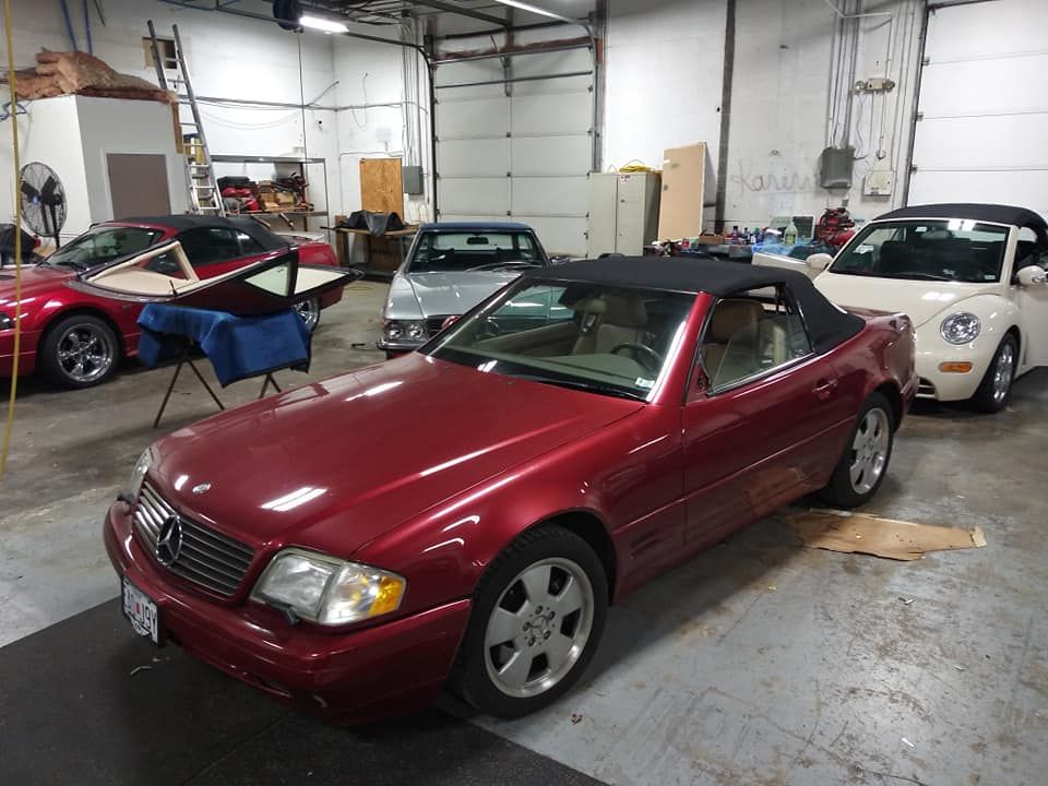 A red Mercedes-Benz convertible parked in a well-lit auto repair shop alongside other vehicles.