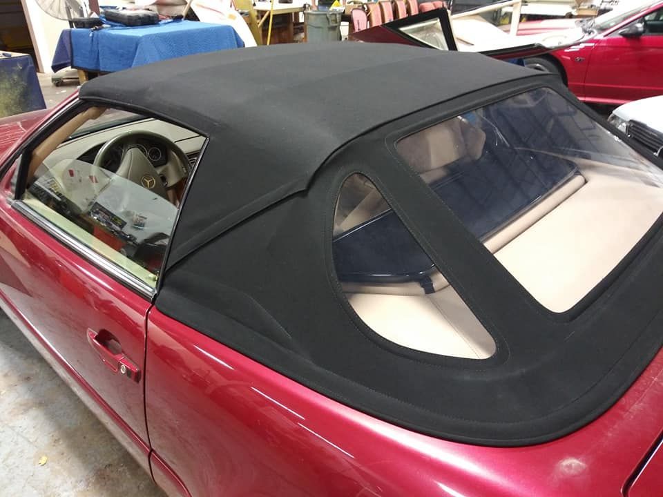A side view of a red convertible car featuring a newly installed, black fabric folding top and a clear plastic window.