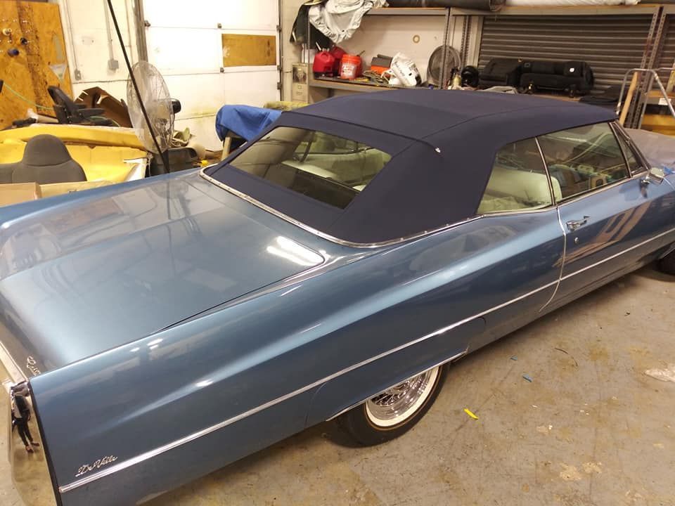 A blue vintage Cadillac convertible with a dark blue fabric top parked in a garage.