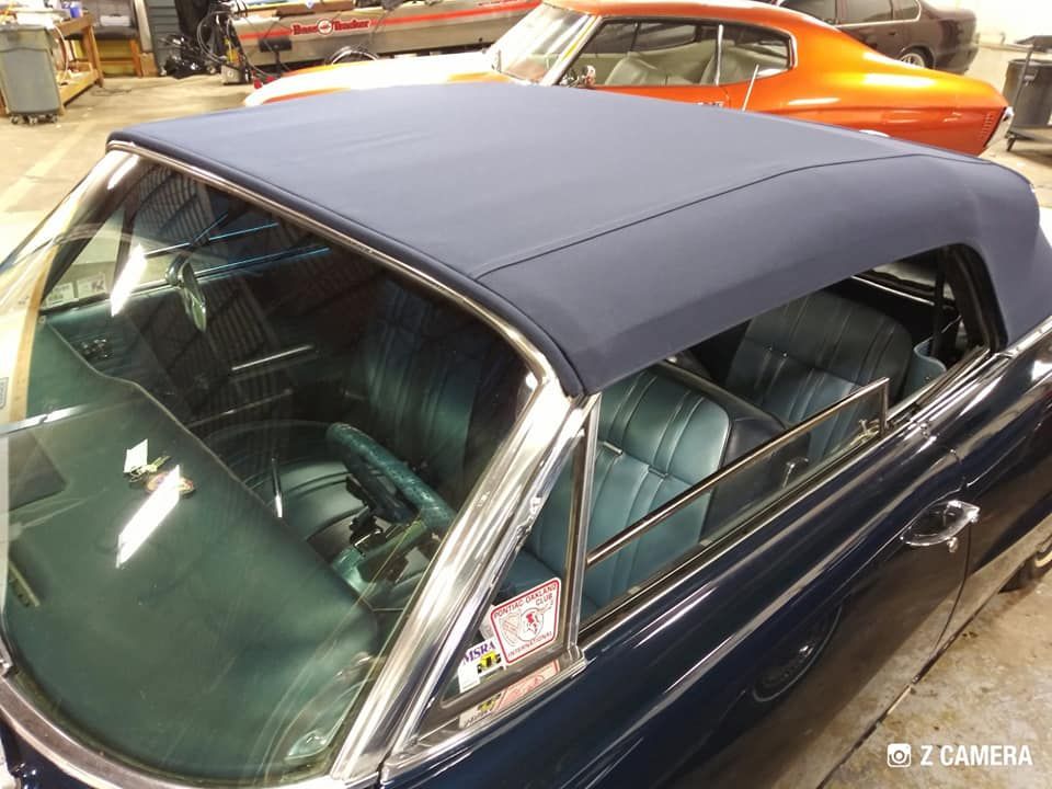 A high-angle view of a dark blue convertible car interior with blue seats, parked in an automotive garage.