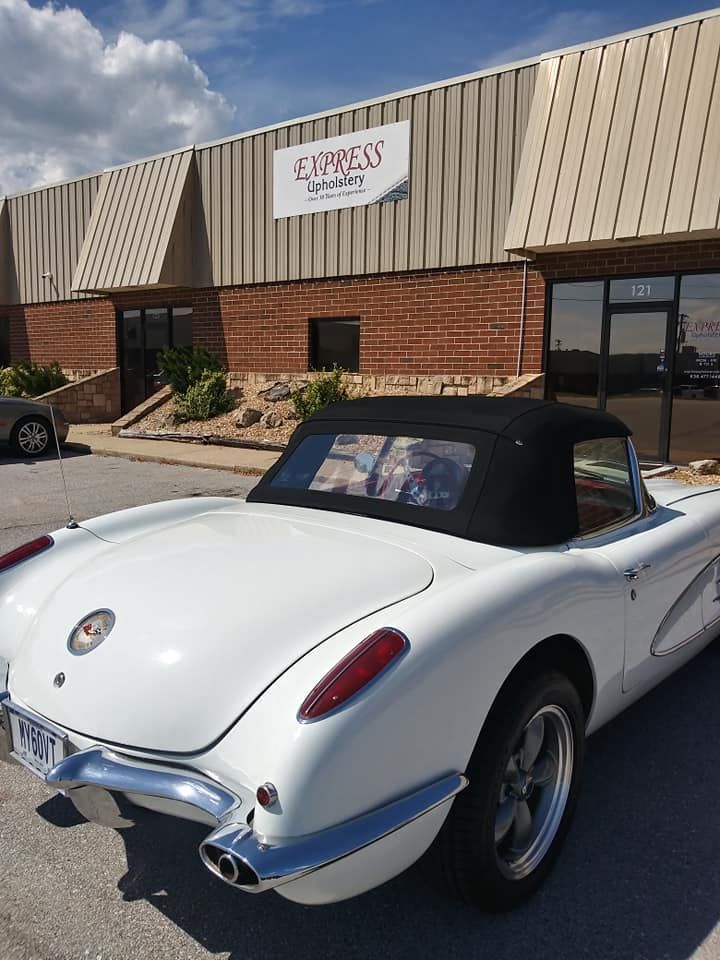 A white vintage convertible Chevrolet Corvette parked outside a building with an Express Auto Care sign.