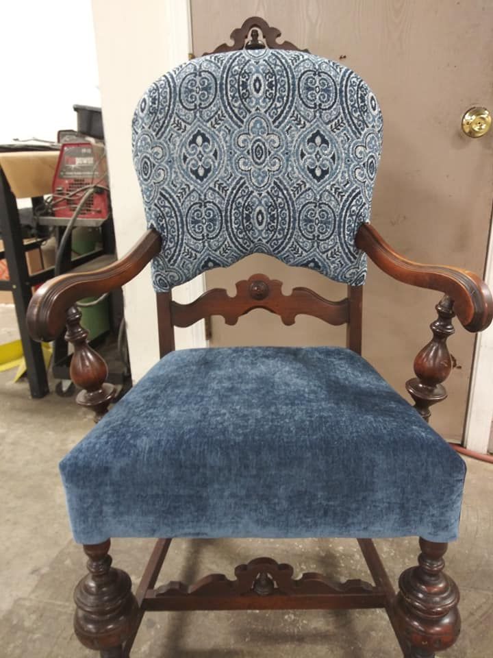 An ornate wooden armchair featuring a patterned blue backrest and a solid blue upholstered seat in a workshop setting.