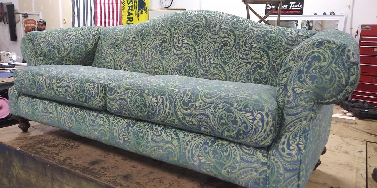 A blue and green paisley upholstered sofa with rolled arms sits on a work platform in a workshop.