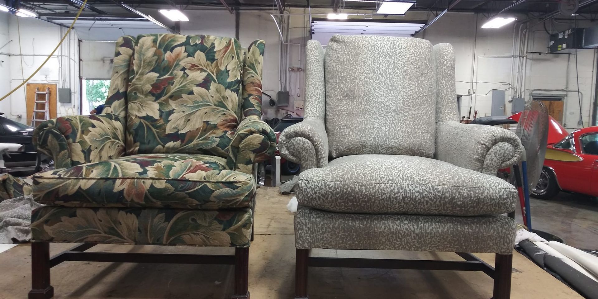 Two wingback chairs side-by-side in a workshop: one upholstered in a floral fabric, the other in a textured gray fabric.