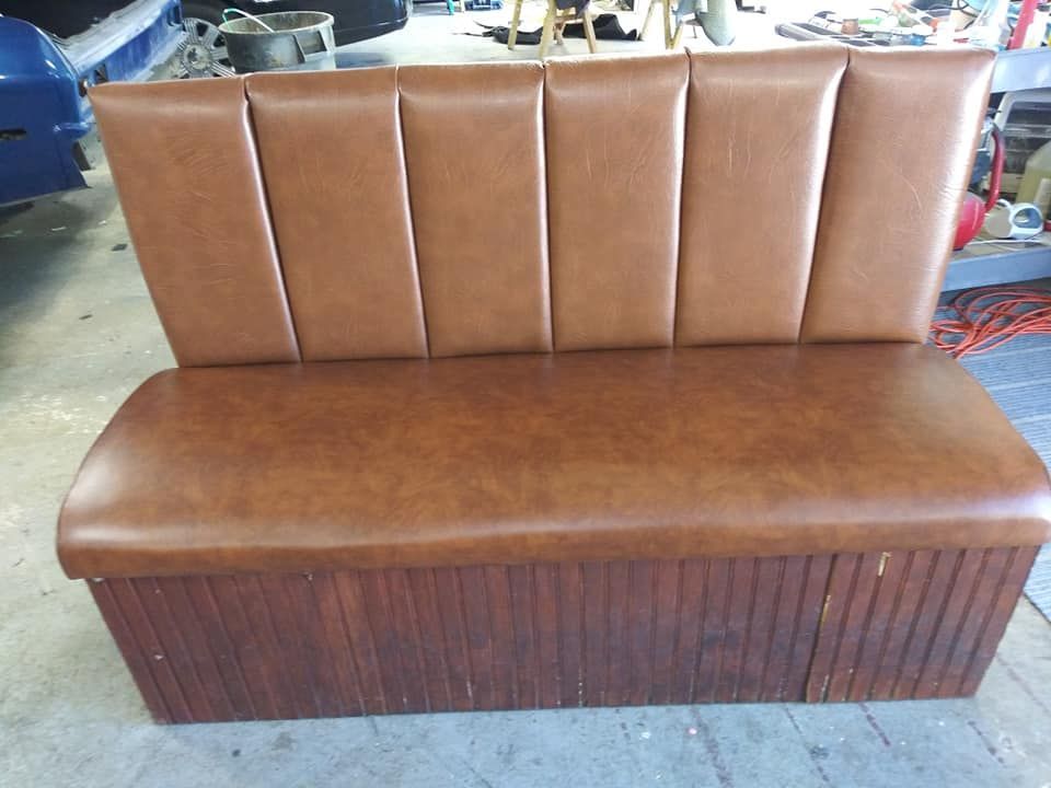 A brown vinyl bench seat with a vertically ribbed backrest and a dark wood-paneled base in a workshop setting.