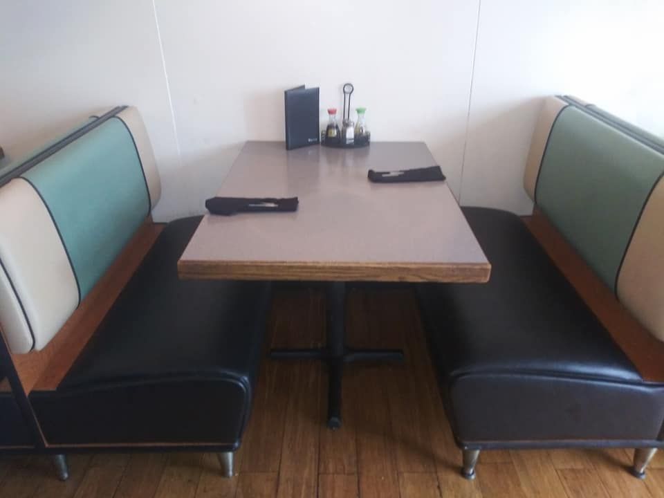 A restaurant booth with black seats, teal and tan backrests, and a wooden table with menus and condiments.