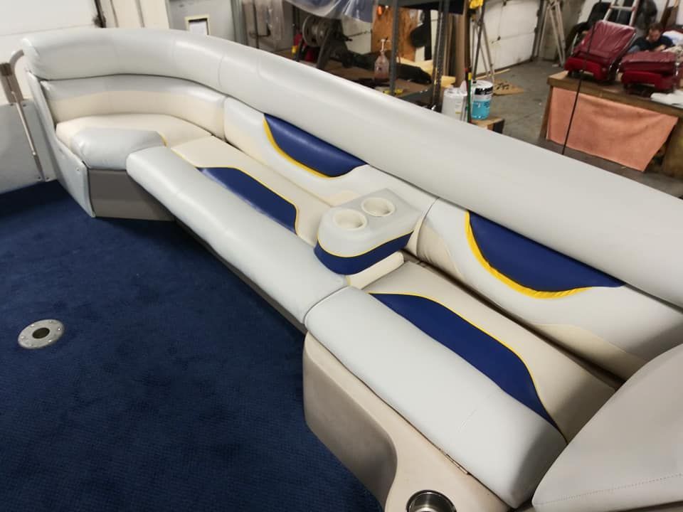 Curved boat seating with white, blue, and yellow vinyl upholstery and a built-in cup holder console on a blue carpet.