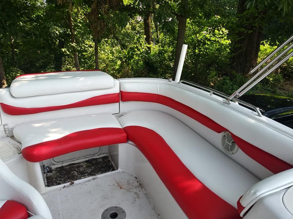 A U-shaped boat seating area with white and red upholstered cushions, set against a background of green trees.