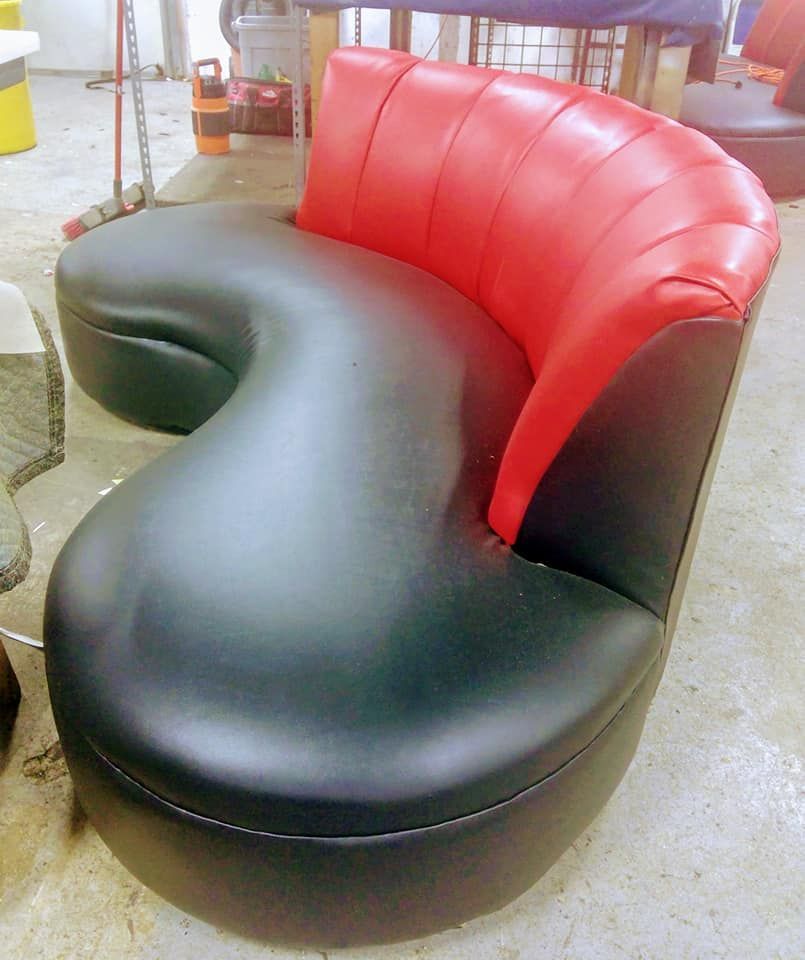 A modern, curved kidney-shaped chair with black upholstery on the seat and a red, vertically stitched backrest.