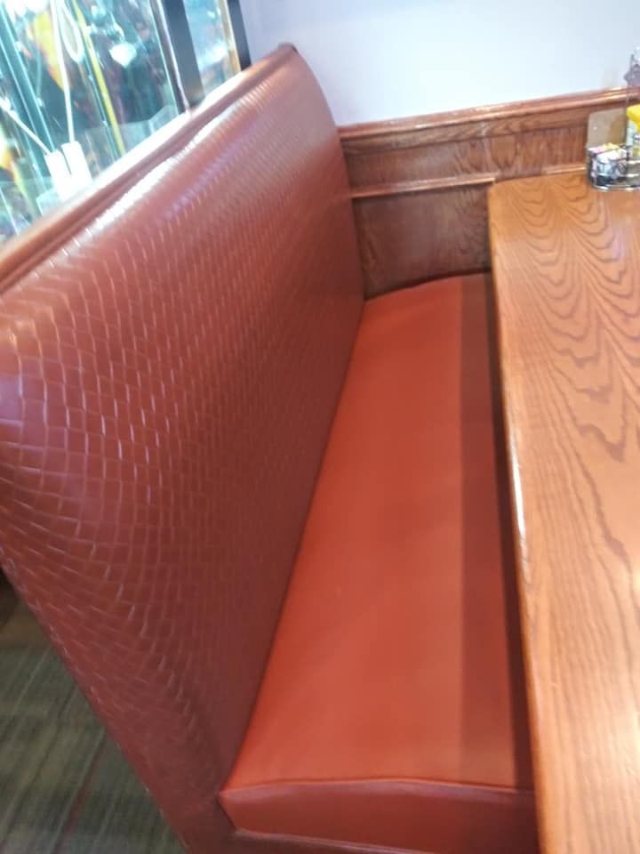 A high-backed restaurant booth featuring a reddish-brown textured backrest, smooth orange seat, and a light wood table.