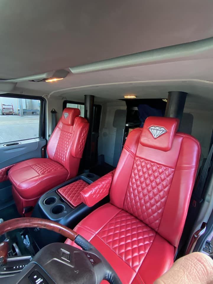 The interior of a vehicle features two vibrant red, diamond-stitched leather captain's chairs with headrest logos.