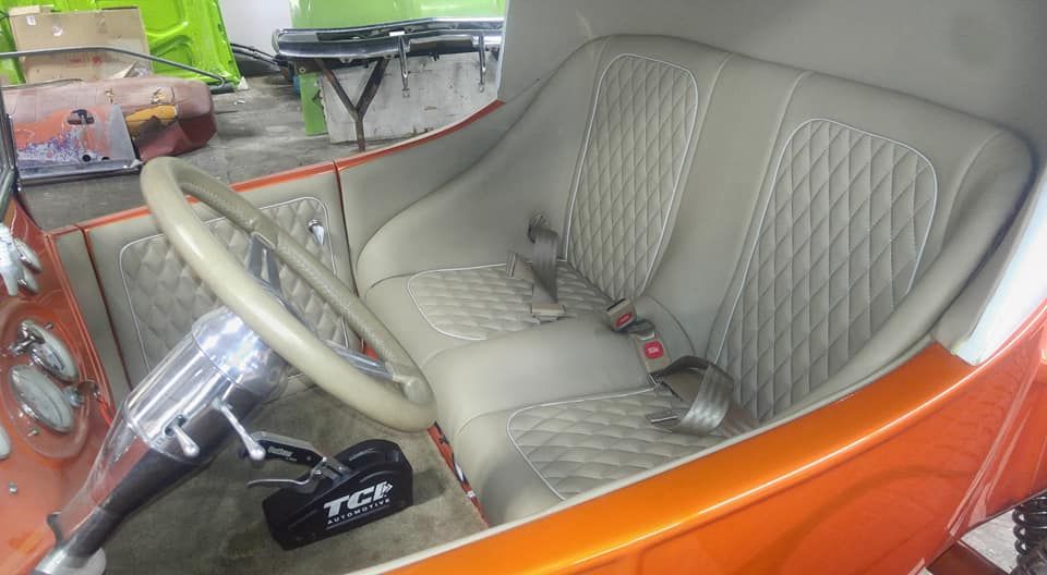 The interior of a custom orange vehicle with light beige diamond-stitched bucket seats and a TCI shifter.