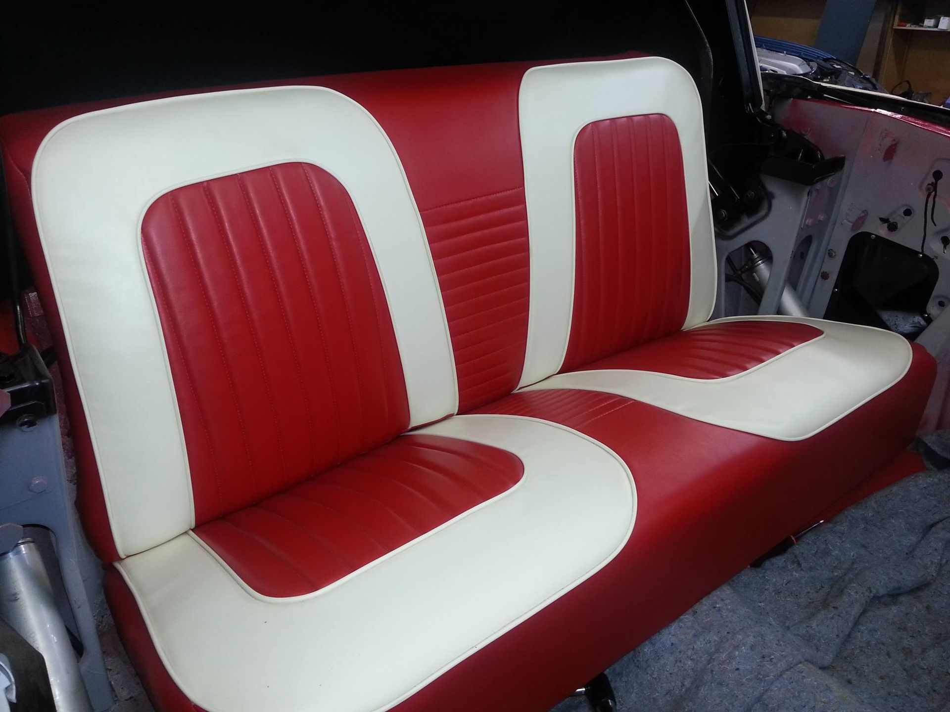 A red and cream-colored upholstered bench seat for a classic car interior.