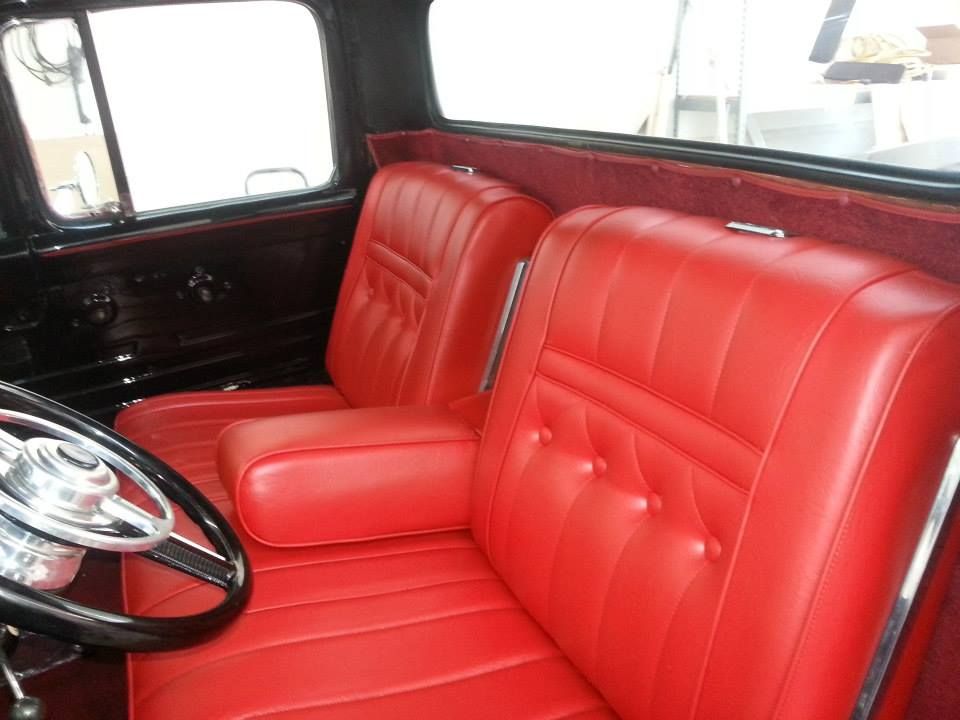 Red bench seat and steering wheel inside a classic truck cab with black doors and red interior trim.