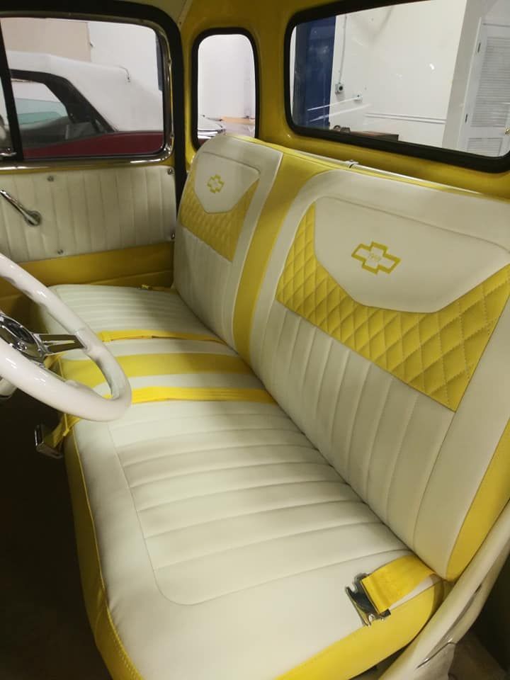 Custom white and yellow bench seat with quilted patterns and Chevrolet emblems inside a classic truck cab.