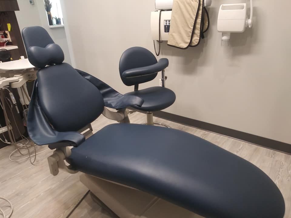 A dental exam chair with dark blue upholstery and a matching operator stool in a clinical office setting.