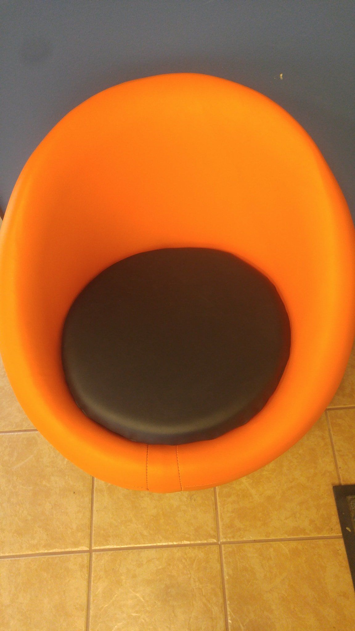 A bright orange rounded lounge chair with a circular black seat cushion sits on a tiled floor.