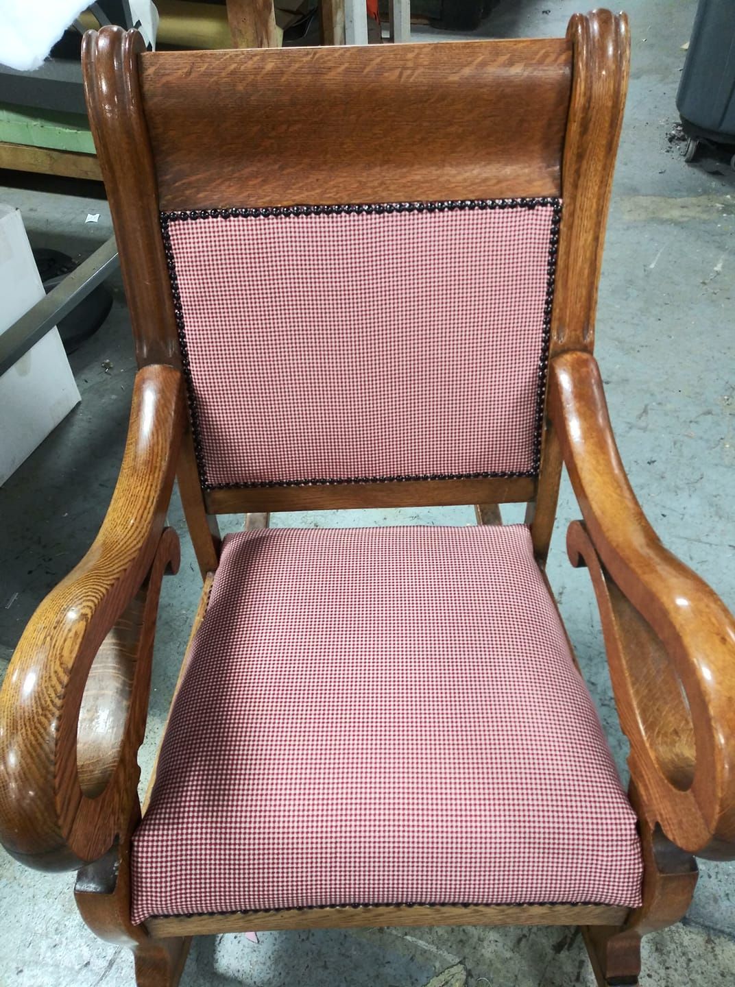 A wooden rocking chair featuring a warm-toned, oak finish and upholstered seat and back cushions in a red gingham fabric.