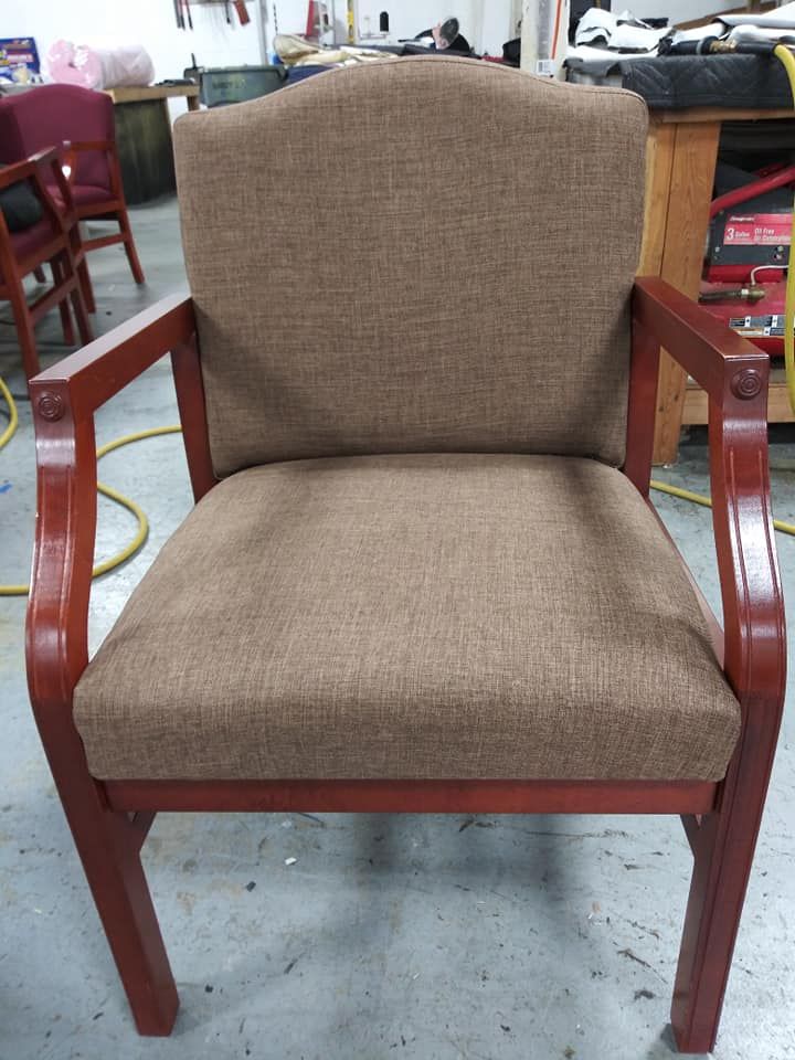 A brown upholstered chair with a curved backrest and stained wooden arms and legs, centered in a workshop setting.