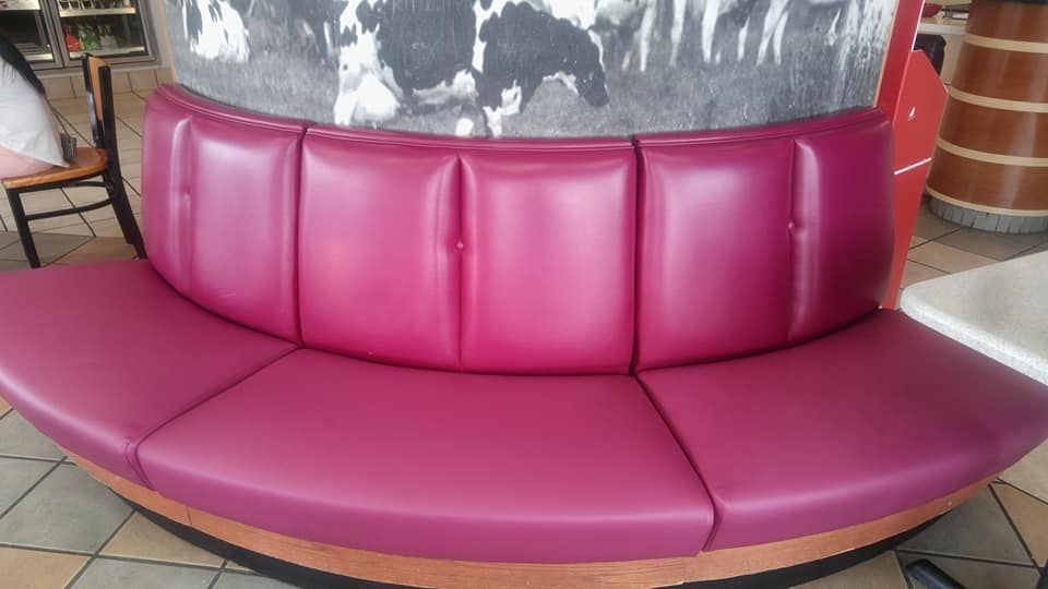 A curved, bright magenta vinyl booth seat sits in front of a wall featuring a black-and-white print of cows.