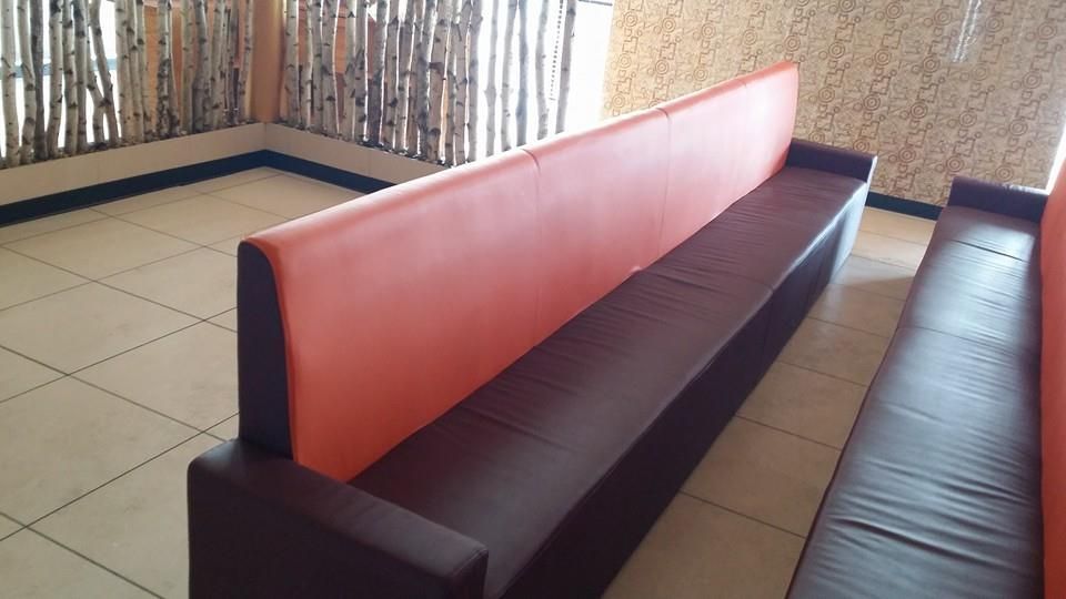 A dual-sided bench seat with brown cushions and orange backrests in a room with a light-tiled floor and rustic walls.