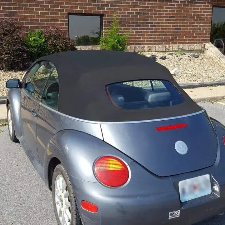 A gray Volkswagen Beetle convertible parked outdoors in front of a brick building.