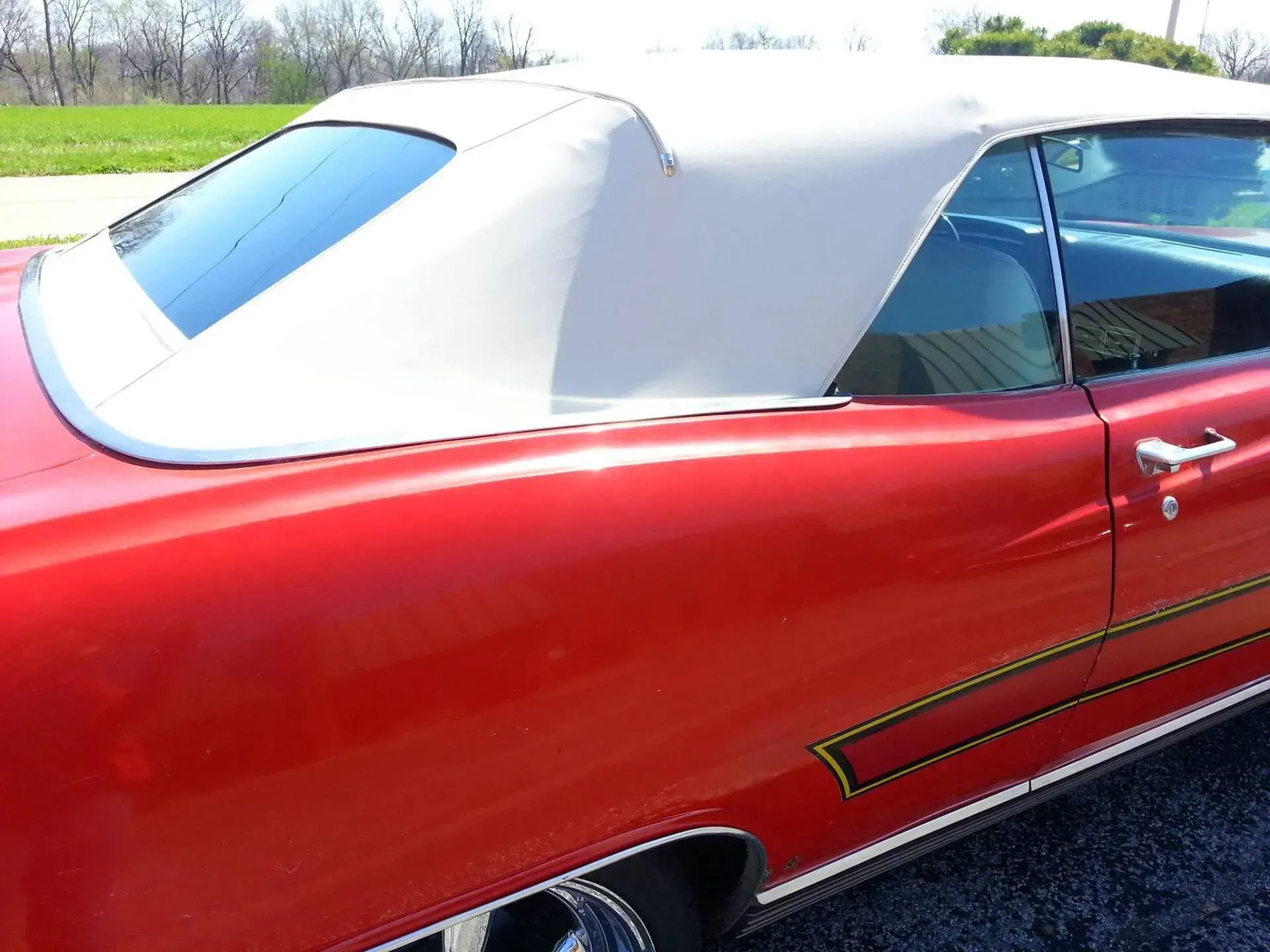 A close-up view of the side of a red convertible car featuring a cream-colored fabric top, parked outdoors.